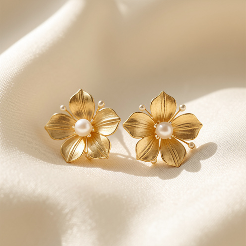 Boucles d’oreilles élégantes en forme de fleurs, ornées de pétales dorés et de délicates perles, présentées sur une soie ivoire.
