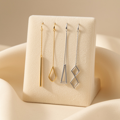Assortiment de boucles d’oreilles pendantes élégantes, aux formes géométriques et allongées, présenté sur un support en velours crème.