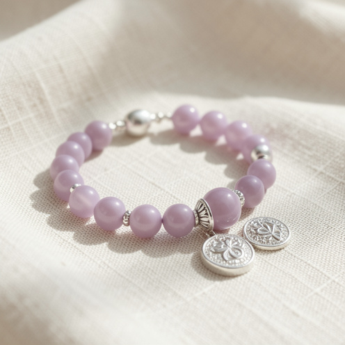 Bracelet mauve délicat présenté avec des bijoux argentés et lavande assortis sur un tissu en lin crème.